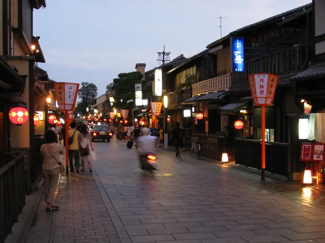 There is a way where there are few vehicles on it and there are few persons and buildings on either...